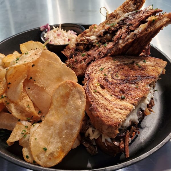 MP Kitchen & Bar's grilled sandwich with pulled meat, melted cheese, chips, and coleslaw.