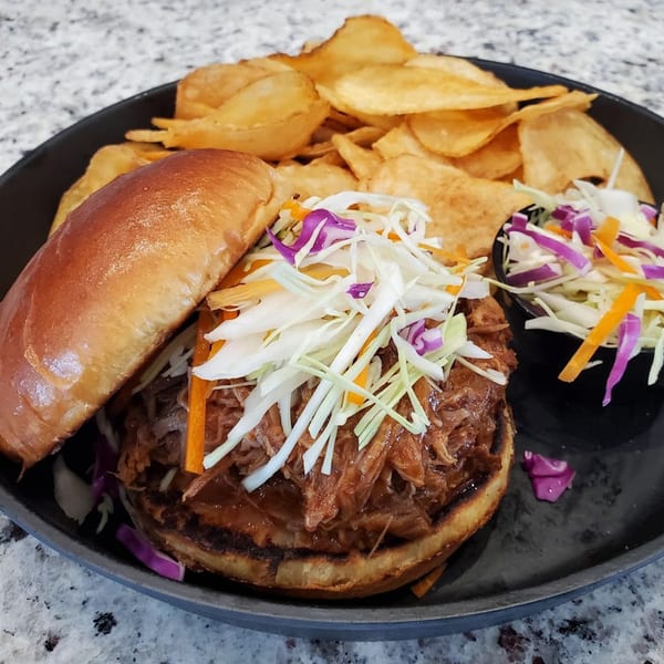Pulled pork sandwich with coleslaw and chips on a dark plate from MP Kitchen & Bar.